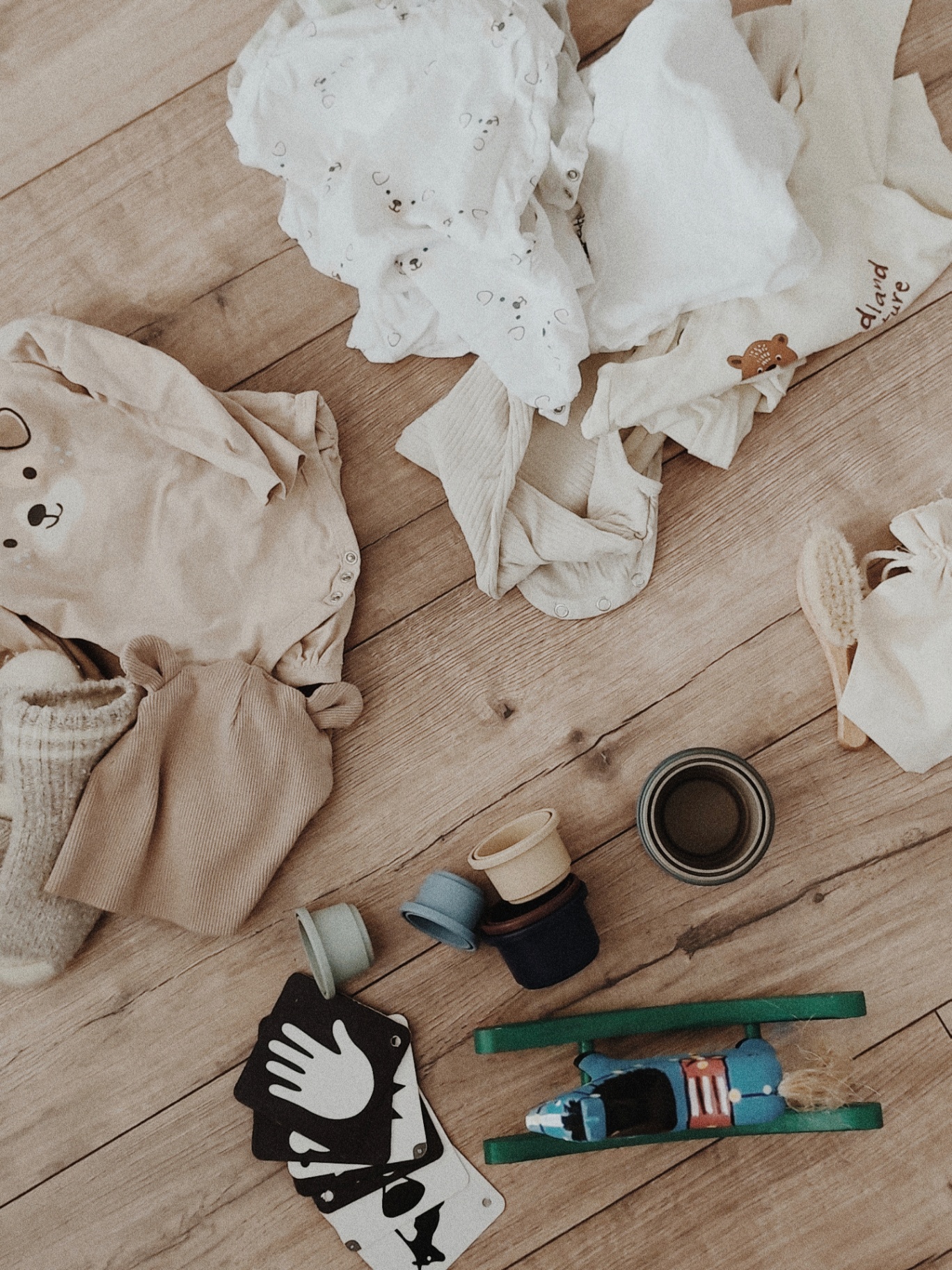 Ubranka i zabawki dla niemowlaka rozłożone na drewnianej podłodze – wyprawka dla bobo